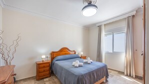 A bedroom with a wooden bed, a nightstand, a dresser, and a window with curtains. - Holiday Home 'Apartamento Bahía Serena Conil' with Wi-Fi (Conil de la Frontera)