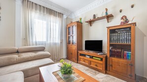 A living room with a sofa, a coffee table with a plant, a television, wooden cabinets, and bookshelves. - Holiday Home 'Apartamento Bahía Serena Conil' with Wi-Fi (Conil de la Frontera)