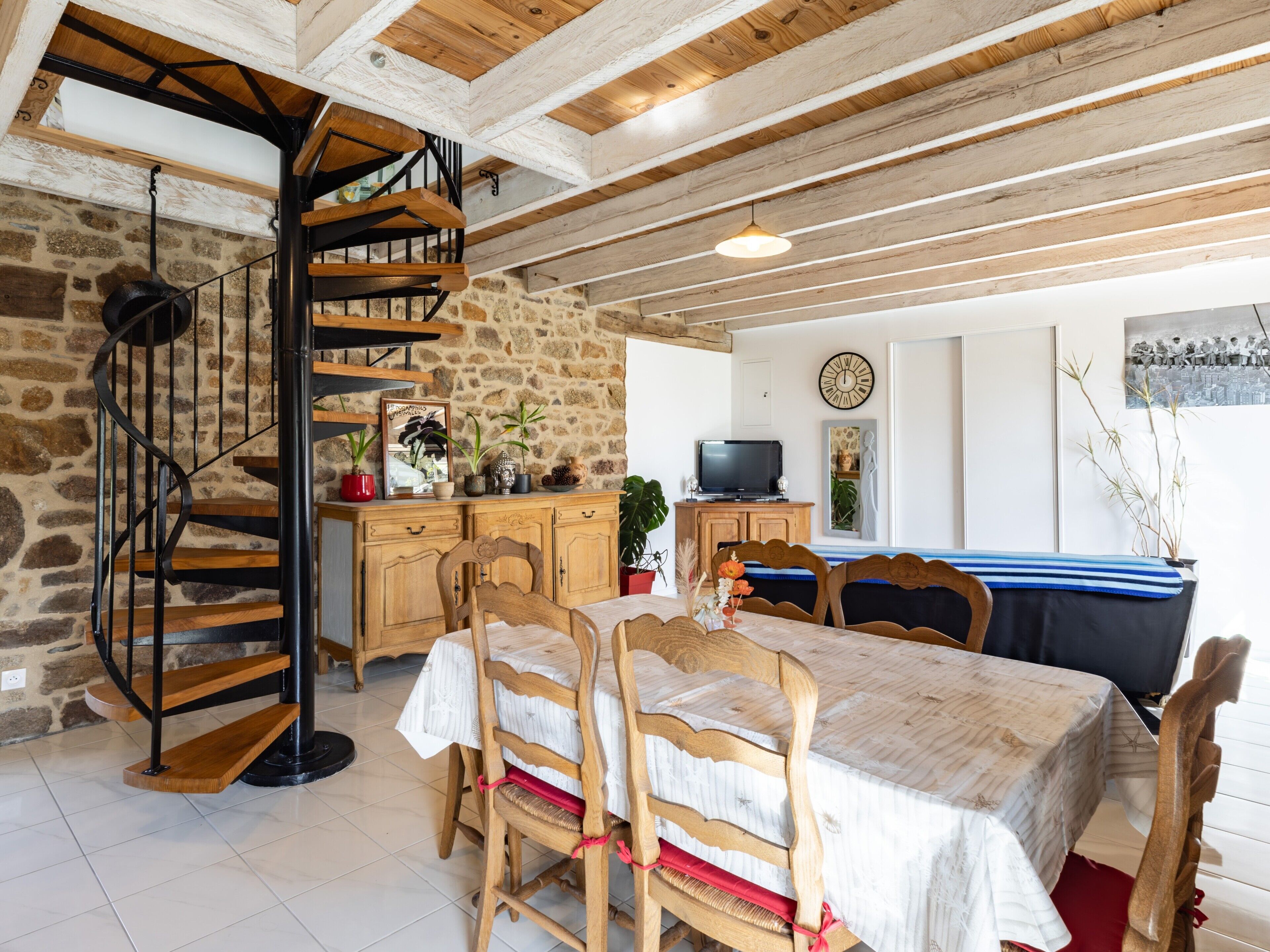 Un interior rústico con una escalera espiral, muebles de madera, paredes de piedra y un comedor.