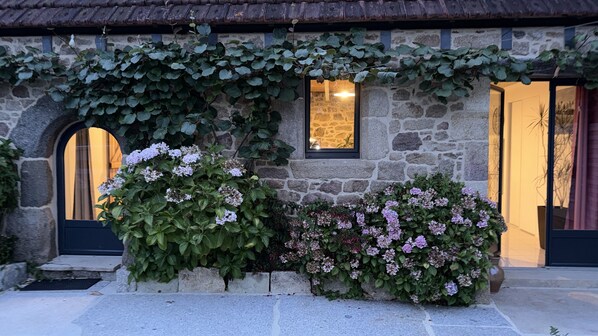 Un edificio de piedra con ventana, puerta y un pequeño jardín con plantas y flores.