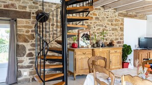 Un escalier en colimaçon avec des marches en bois et des rampes en métal noir, un meuble en bois orné d’objets décoratifs et une table à manger avec des chaises.
