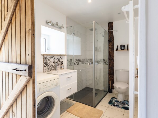 Une salle de bain moderne avec une douche à parois de verre, un lave-linge et des toilettes.