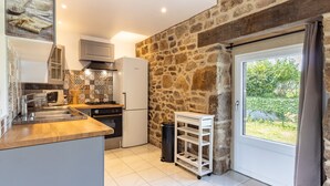 Une cuisine avec un mur en pierre, un four encastré, un évier et une fenêtre donnant sur un paysage verdoyant.
