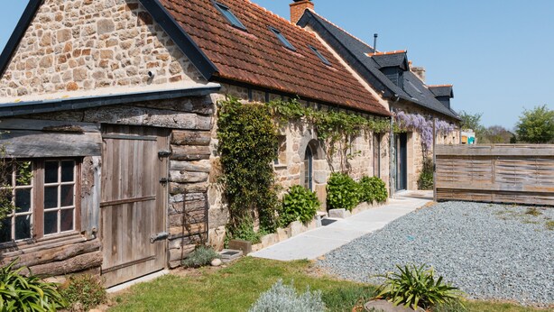 Un bâtiment en pierre avec un toit en pente, une porte en bois et une allée gravillonnée.