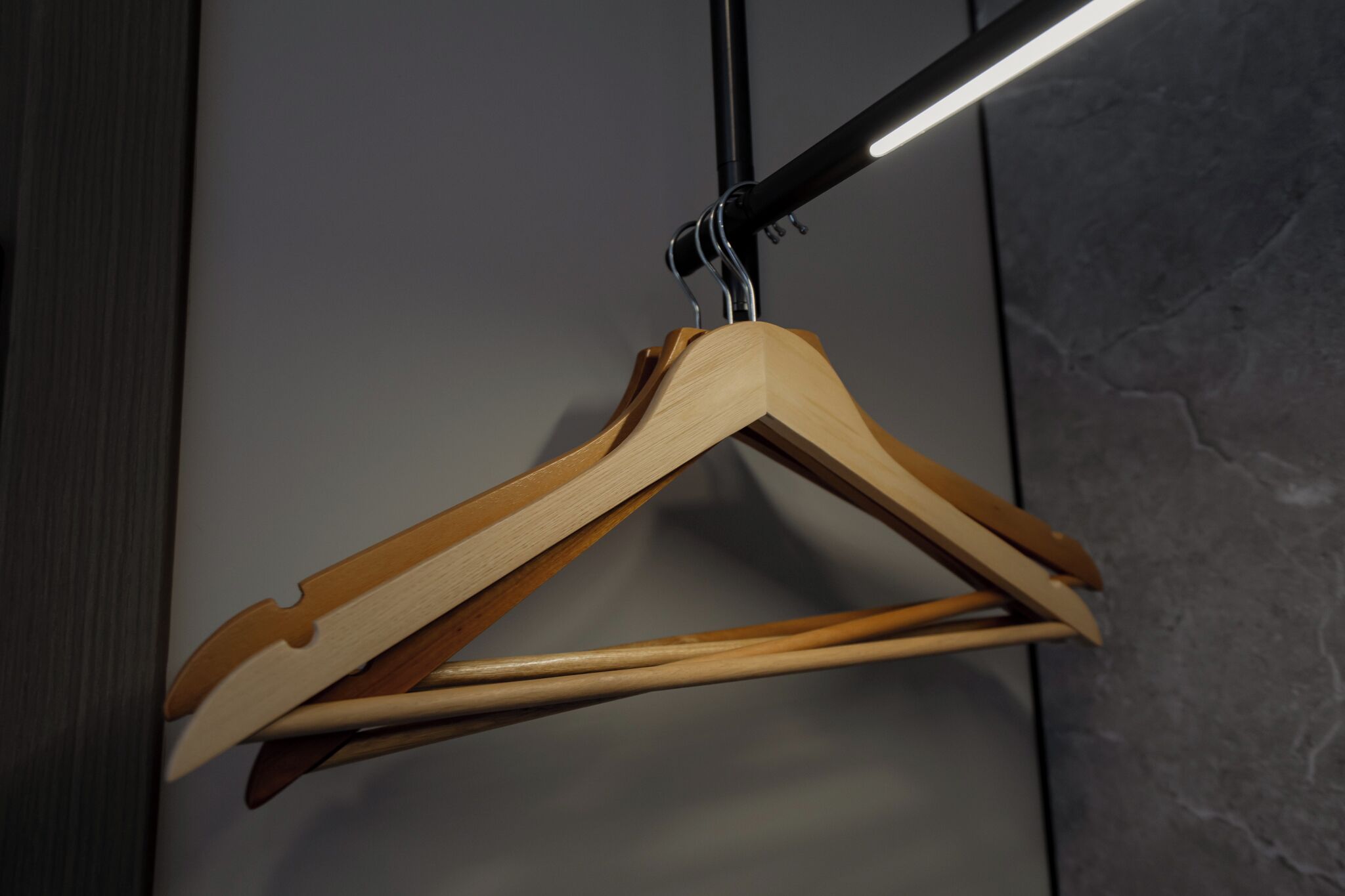 A wooden hanger with a metal hook against a grey wall.