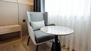 A modern room with a grey upholstered armchair, a round table, a wooden bench, and a window with sheer curtains. - HippoTel Khaorang Phuket Town (Phuket)
