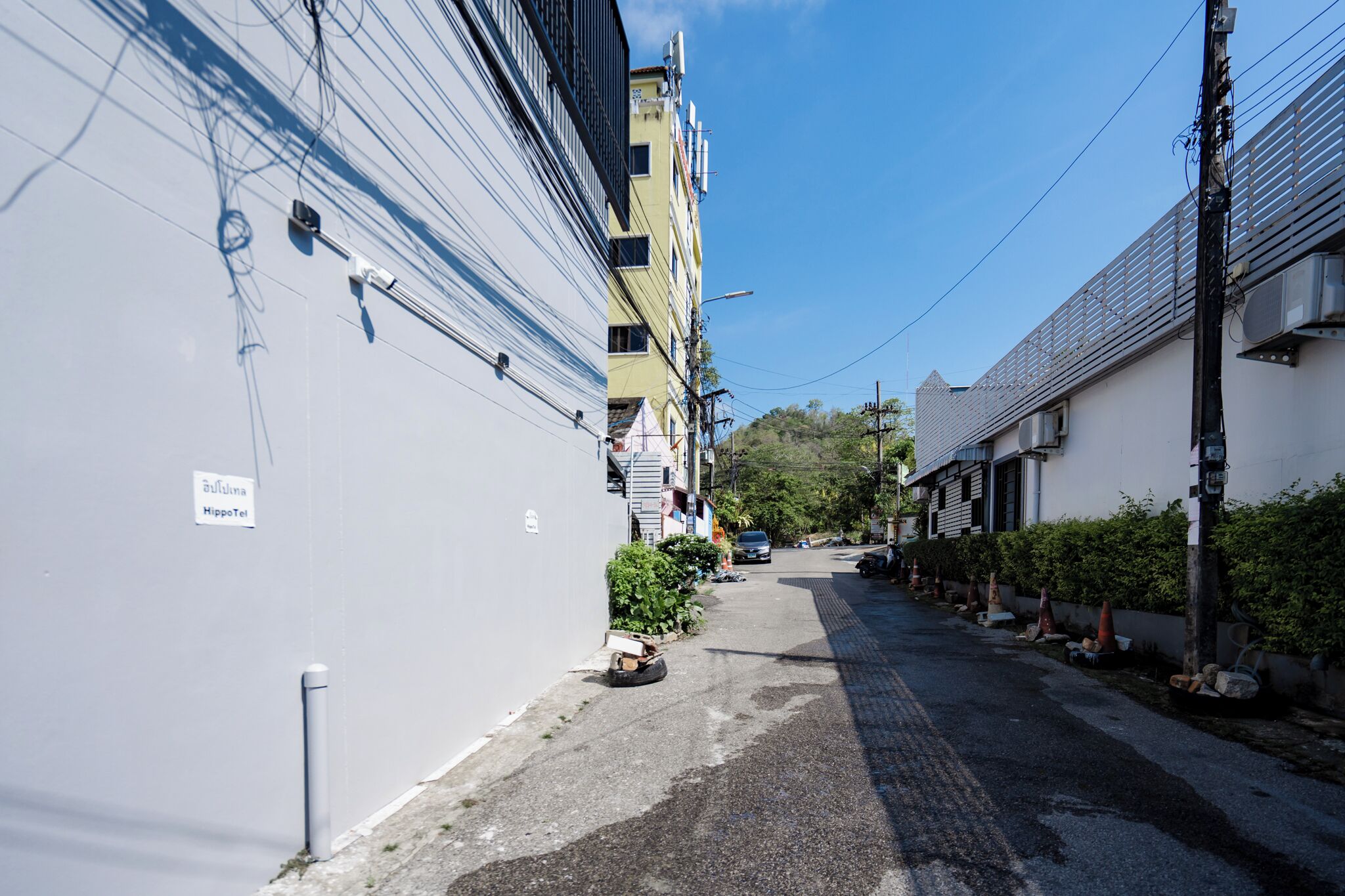 A narrow urban street with buildings on both sides, a clear sky, and a sign indicating a HippoTel service.