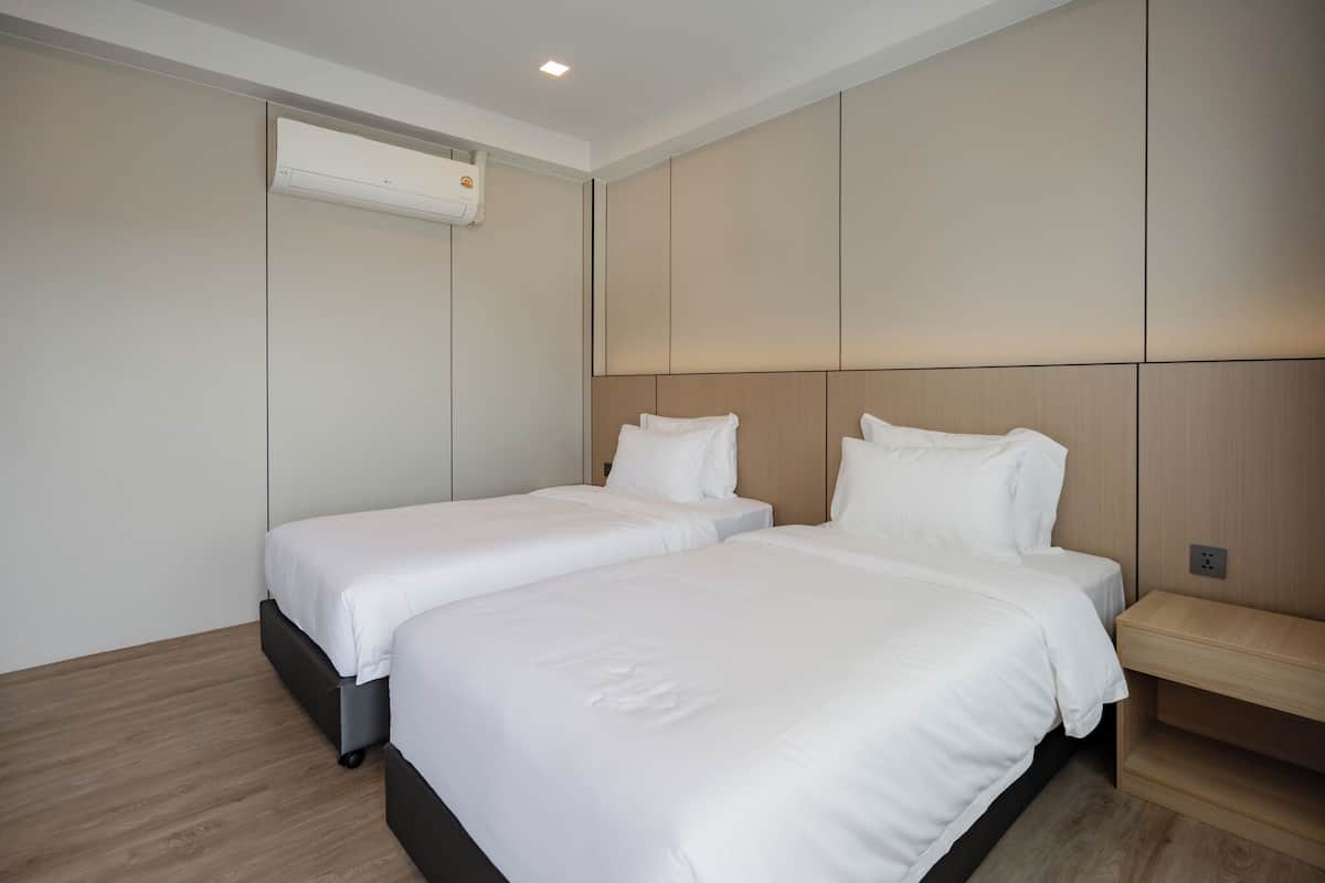 Une chambre d’hôtel avec deux lits, un plancher en bois, un climatiseur fixé au mur et une table de chevet.