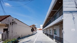 A corridor with a concrete floor, blue railings, and buildings on either side. - HippoTel Khaorang Phuket Town (Phuket)