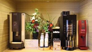 A hotel room with a minibar, a coffee machine, and a flower arrangement.