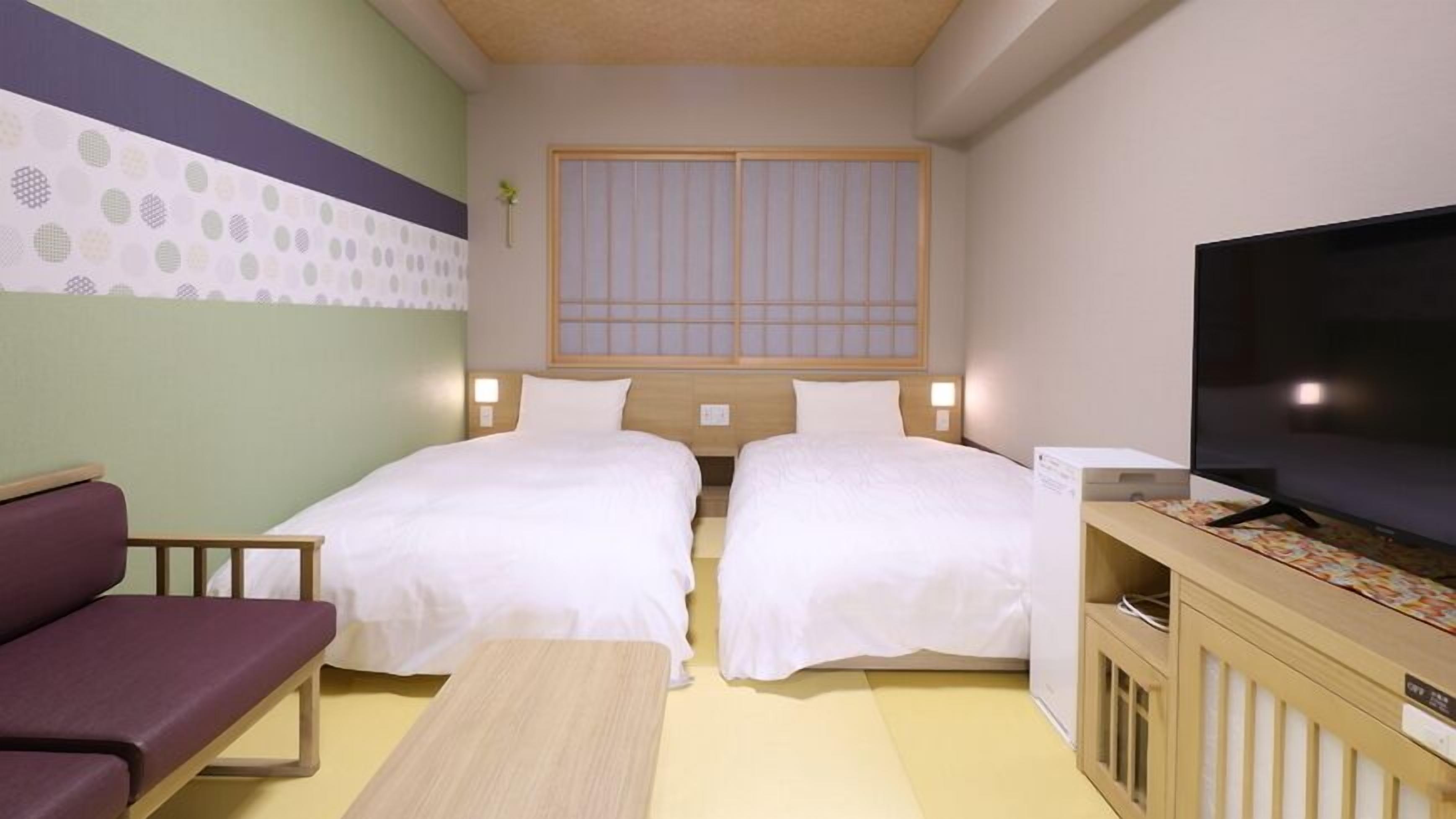 Una habitación de hotel con dos camas, televisión, escritorio y sofá.
