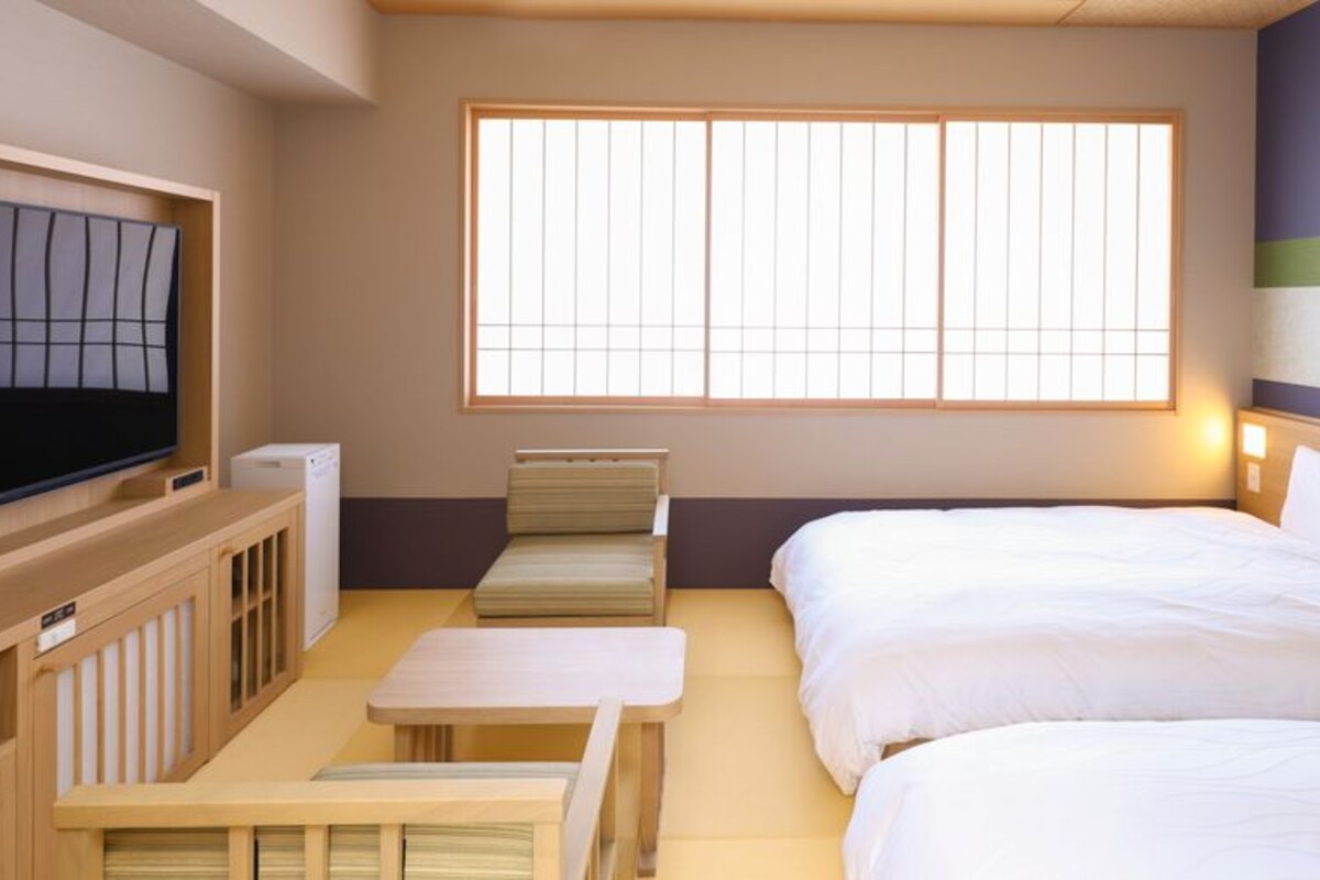 Una habitación de hotel con cama, televisión, una mesita y una ventana con persianas.