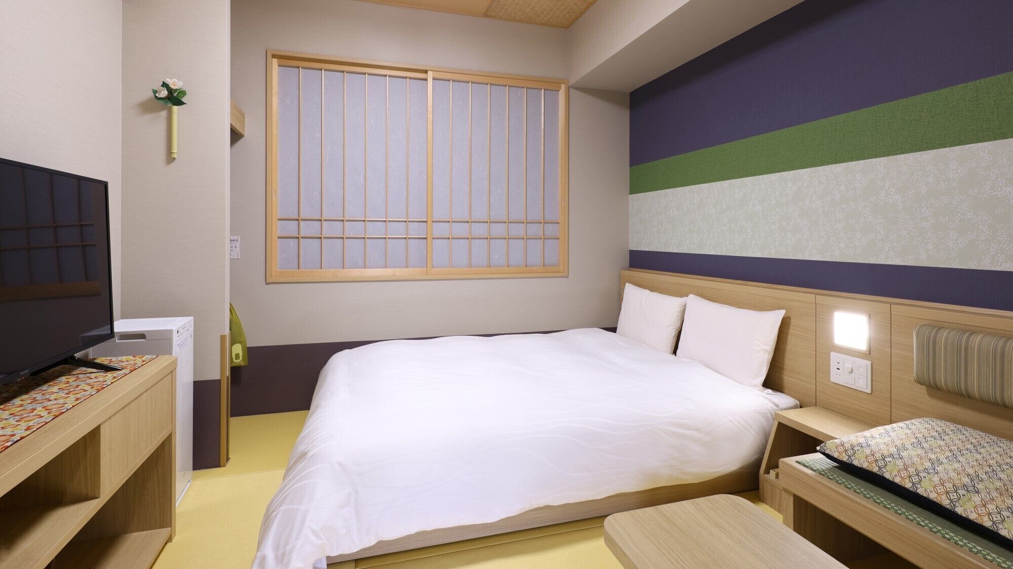 Habitación de hotel con cama, mesita de noche, televisor y ventana con persianas verticales.