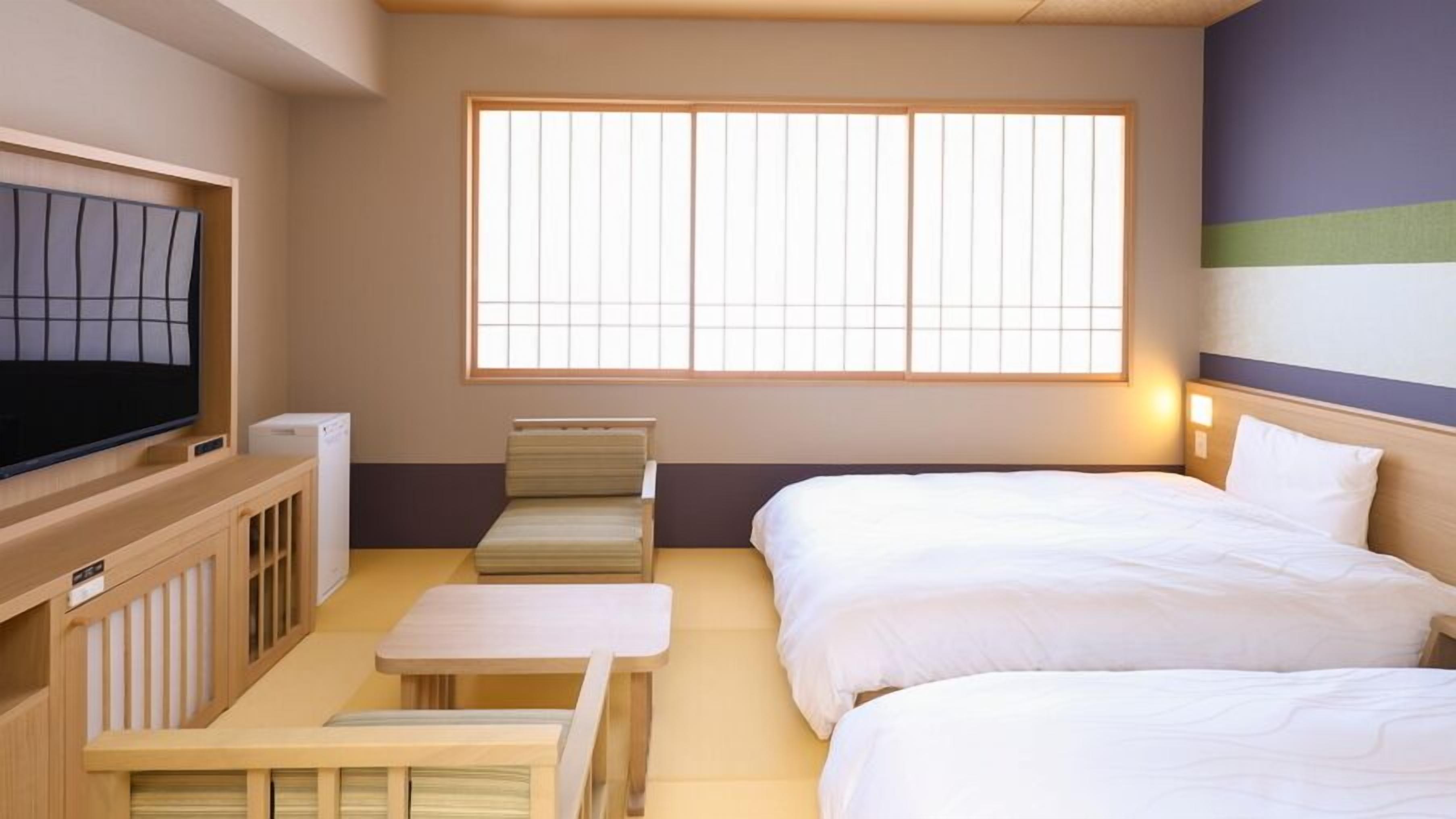 Una habitación de hotel con cama, televisión, una mesita y una ventana con persianas.