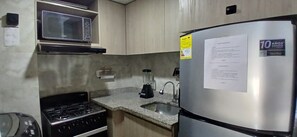 A kitchen with a microwave, stove, refrigerator, and granite countertop.