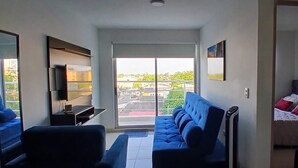 Ett kompakt vardagsrum med en soffa, ett litet bord, en tv och en balkong med utsikt över staden.