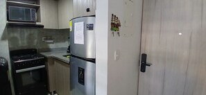 A kitchen with a microwave, stove, refrigerator, and a door with a lock.