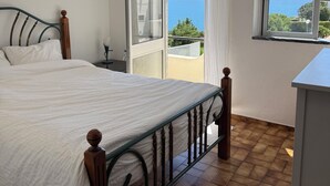 A bedroom with a bed, a window with a view of the sea, and a balcony. - Oceanfront house in Benagil (Lagoa)