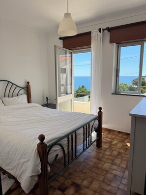 A bedroom with a bed, a window with a view of the sea, and a balcony. - Oceanfront house in Benagil (Lagoa)