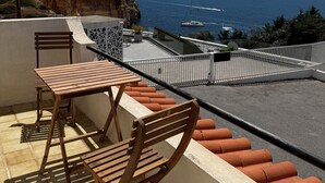 A balcony with a table and chairs, overlooking a coastal area with cliffs and the sea. - Oceanfront house in Benagil (Lagoa)