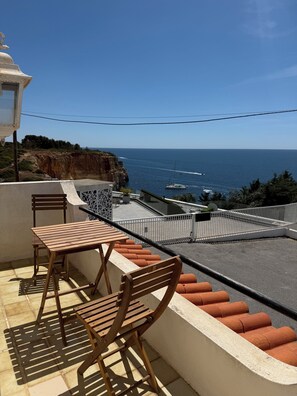 A balcony with a table and chairs, overlooking a coastal area with cliffs and the sea. - Oceanfront house in Benagil (Lagoa)