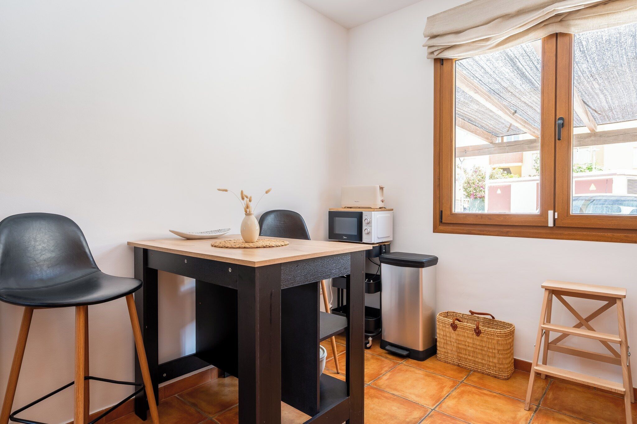 A small room with a table, two chairs, a TV, a trash bin, a wicker basket, and a wooden ladder.