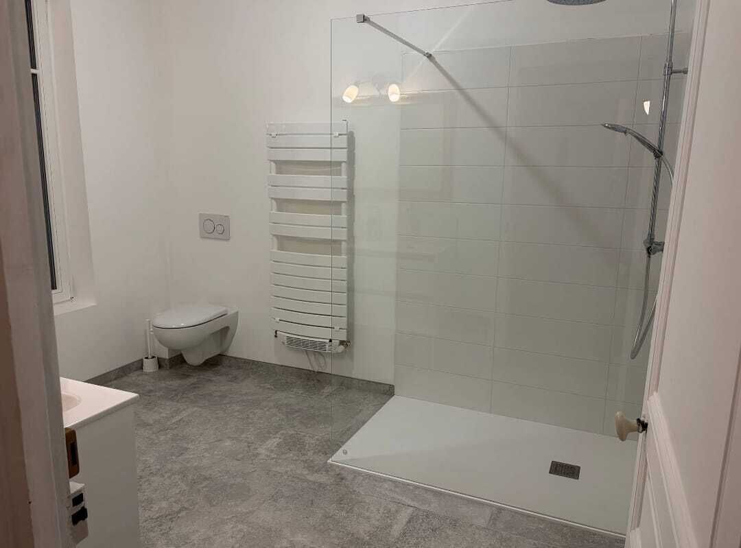 Une salle de bain moderne avec une douche à parois de verre, des toilettes et un porte-serviettes.