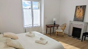 Una habitación de hotel con cama, una silla, una mesa, una chimenea y un cuadro en la pared.
