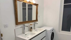Un baño con tocador blanco, espejo con marco dorado, lavadora y ventana.