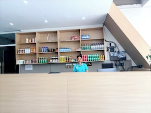 A reception desk with a person standing behind it, shelves stocked with beverages, and a monitor displaying a video. - GUI ZHI HOTEL Koh Rong (Koh Rong)