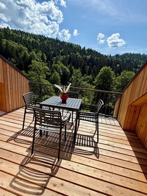 A wooden deck with a table and chairs, overlooking a forested hillside. - Moonlight Soul (Triberg) - Loggia and sauna (Triberg im Schwarzwald)
