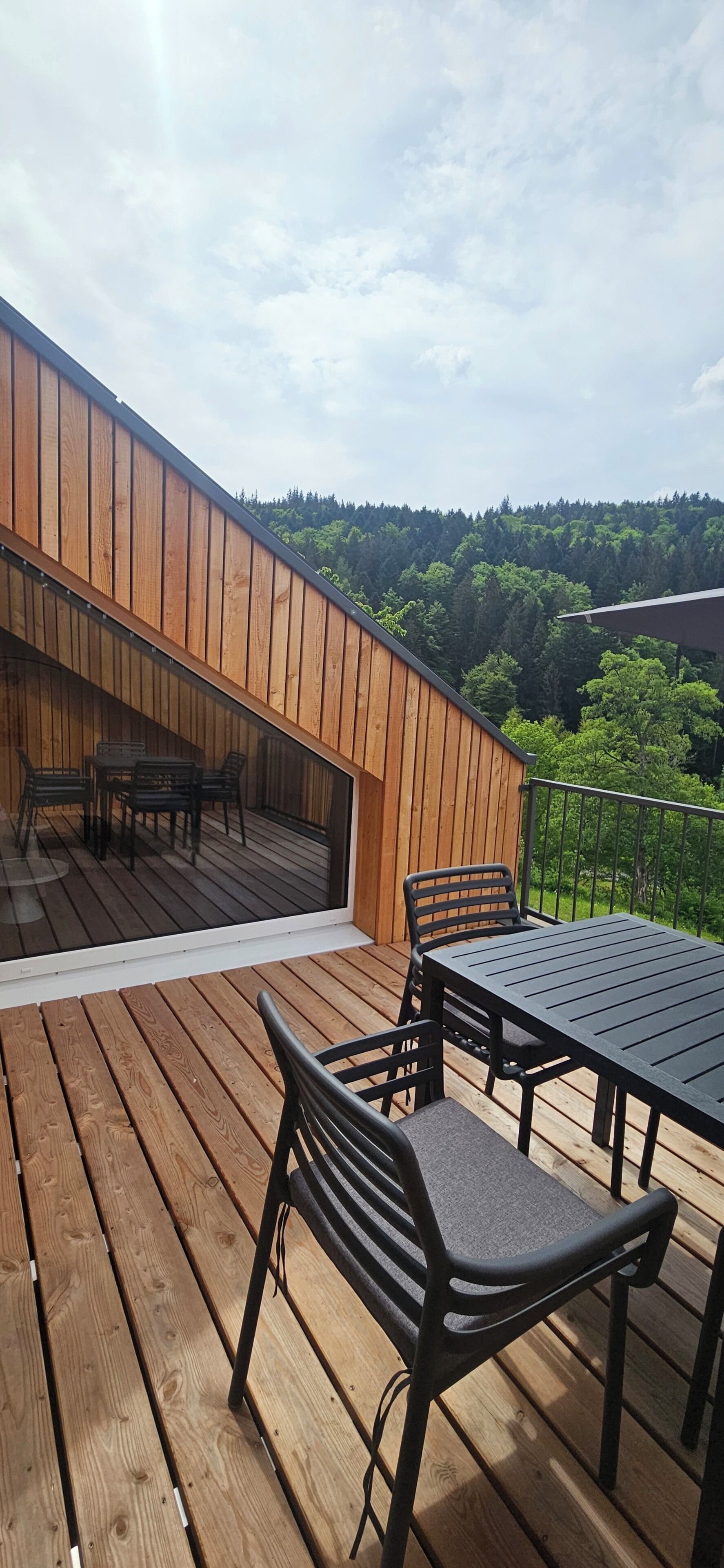 Eine Holzterrasse mit Tisch und Stühlen mit Blick auf einen bewaldeten Hang.