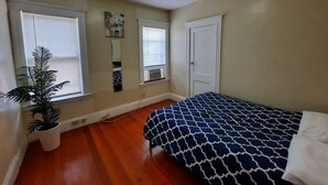 Une chambre à coucher avec un lit, deux fenêtres, une plante en pot et une porte.