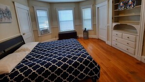 Une chambre à coucher comprenant un lit, un radiateur, une fenêtre, une armoire et une étagère avec des objets décoratifs.