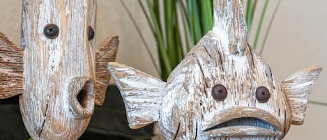 Dos decoraciones rústicas con forma de pez, con ojos de metal y una planta al fondo.
