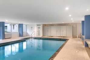Une piscine dotée d’une terrasse carrelée, d’un espace vestiaire et offrant une vue sur l’extérieur.