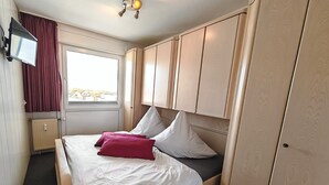 Un dormitorio con cama, televisión, ventana y armario.