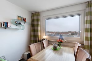 Un coin repas avec une table en bois, des chaises, un vase de fleurs et une fenêtre avec des rideaux.