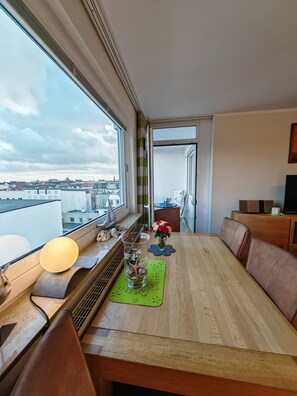 Uma área de refeições com vista para a cidade, uma mesa com cadeiras, um vaso com flores e um abajur.