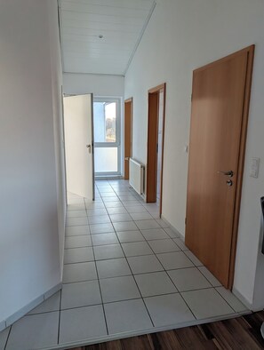 A hallway with white tiled flooring, wooden doors, and a radiator. - Vacation assembly apartment 2 bedrooms 3 beds A30 (Ibbenbüren)