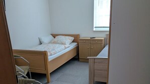 Ein kleines, aufgeräumtes Schlafzimmer mit einem Bett, einem Stuhl, einem Schreibtisch und einem Kleiderschrank.