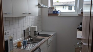 Eine kompakte Küche mit weißen Schränken, einem Einbauofen, einer Kaffeemaschine und einem Fenster mit Blick auf ein Haus.