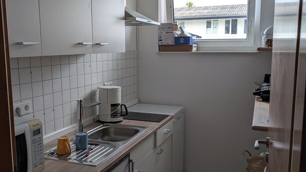 A compact kitchen with white cabinets, a built-in oven, a coffee maker, and a window with a view of a house. - Vacation assembly apartment 2 bedrooms 3 beds A30 (Ibbenbüren)
