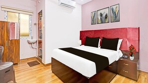 A bedroom with a bed, bedside table, nightstand, and a window with blinds. - Hotel O Ramarvapadu Near ESI Hospital (Penumuluru)