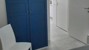 Huoneessa on valkoinen tuoli, sininen vaatekaappi ja valkoinen ovi.