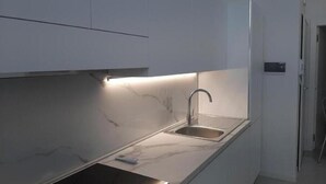 Moderni keittiö, jossa on ruostumattomasta teräksestä valmistettu allas, valkoiset kaapit ja kaappien alaosassa oleva valaistus.