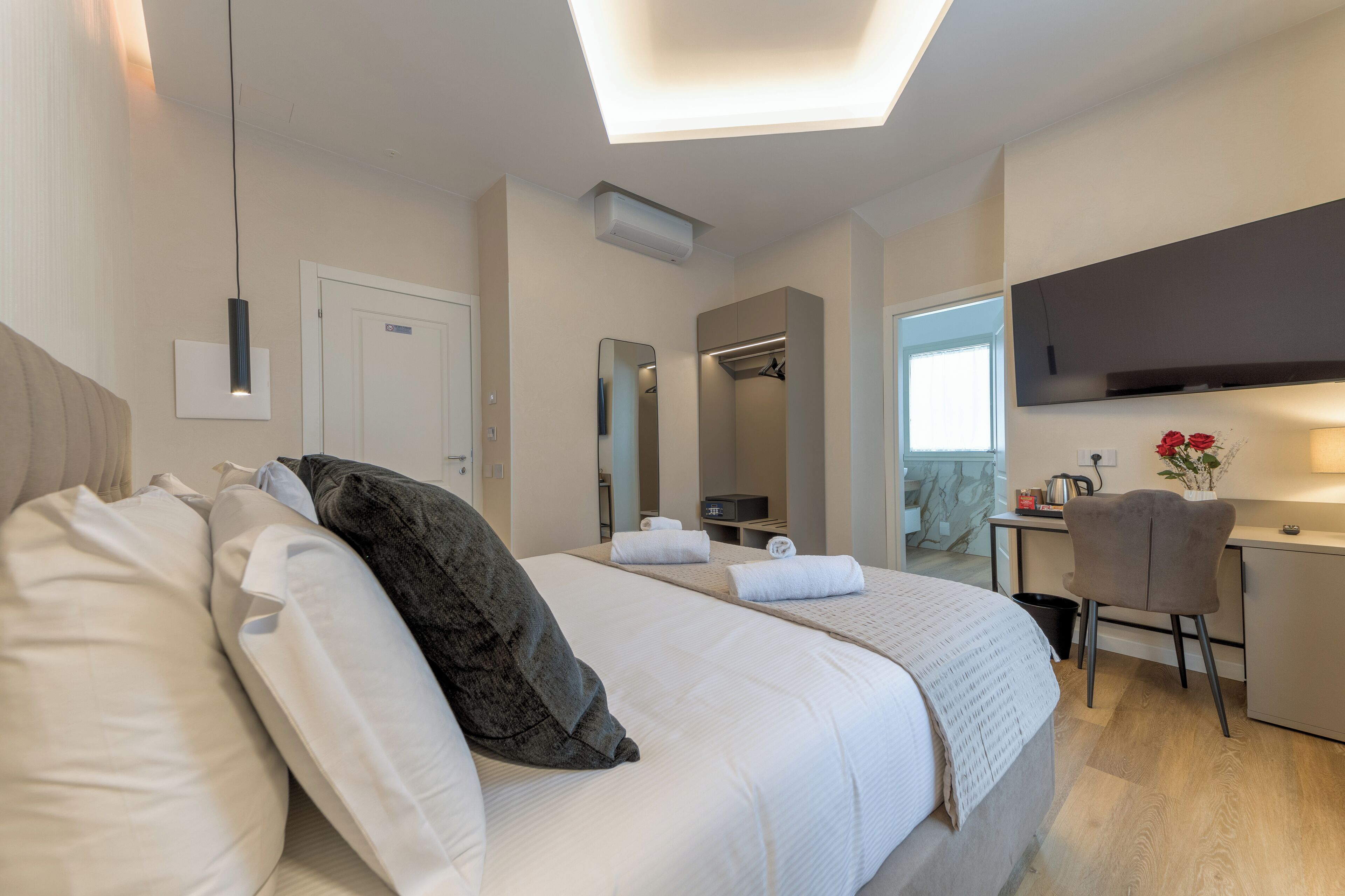A hotel room with a bed, a desk, a chair, a TV, and a mirror.