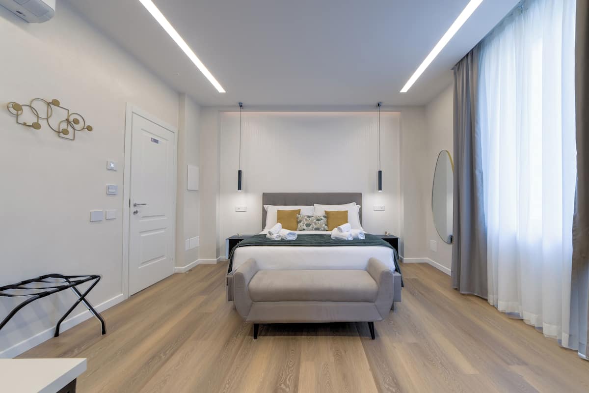 A modern hotel room with a bed, bedside tables, a desk, and a large window with curtains.