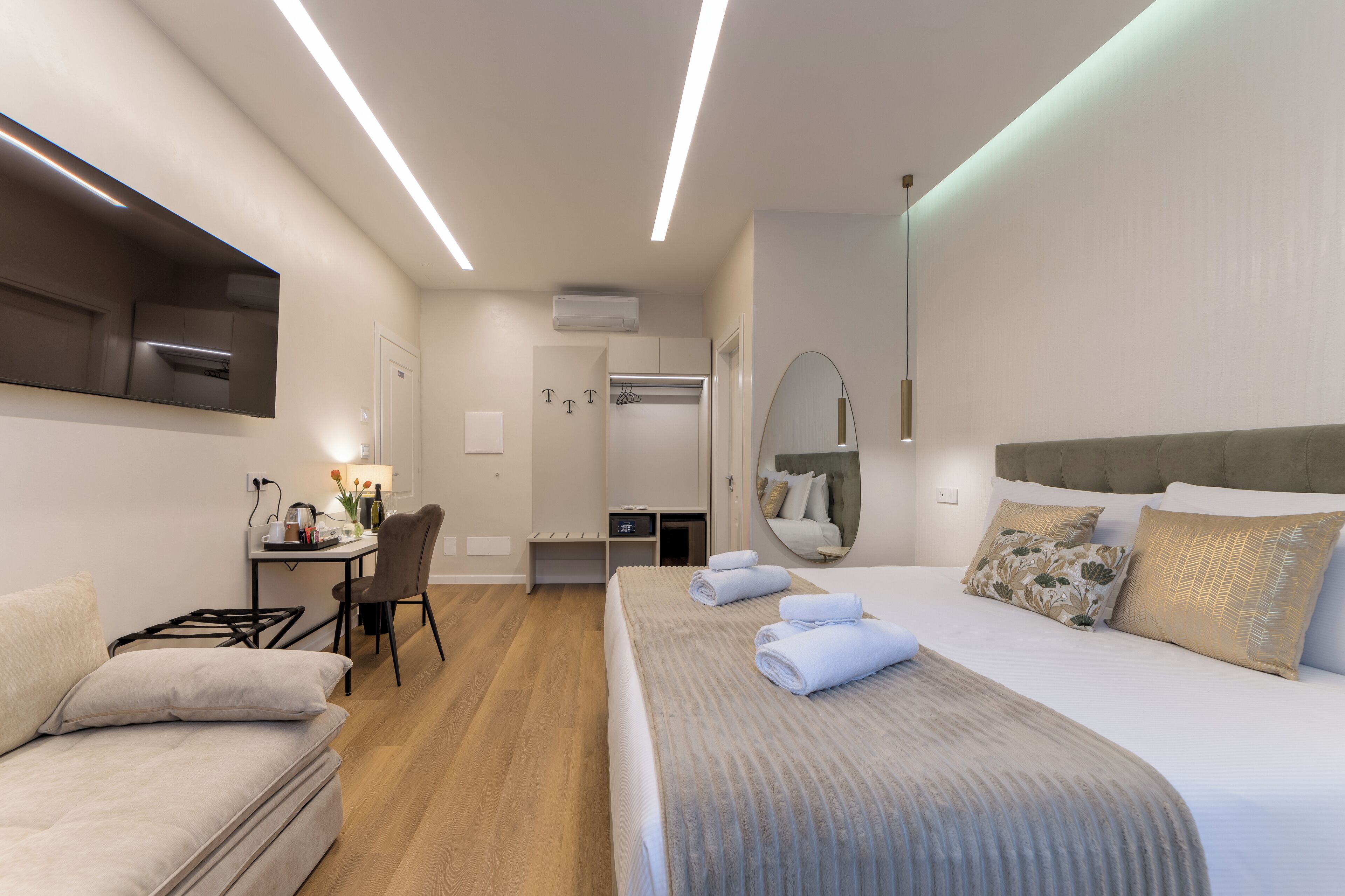 A modern hotel room with a bed, a desk, a chair, and a mirror.