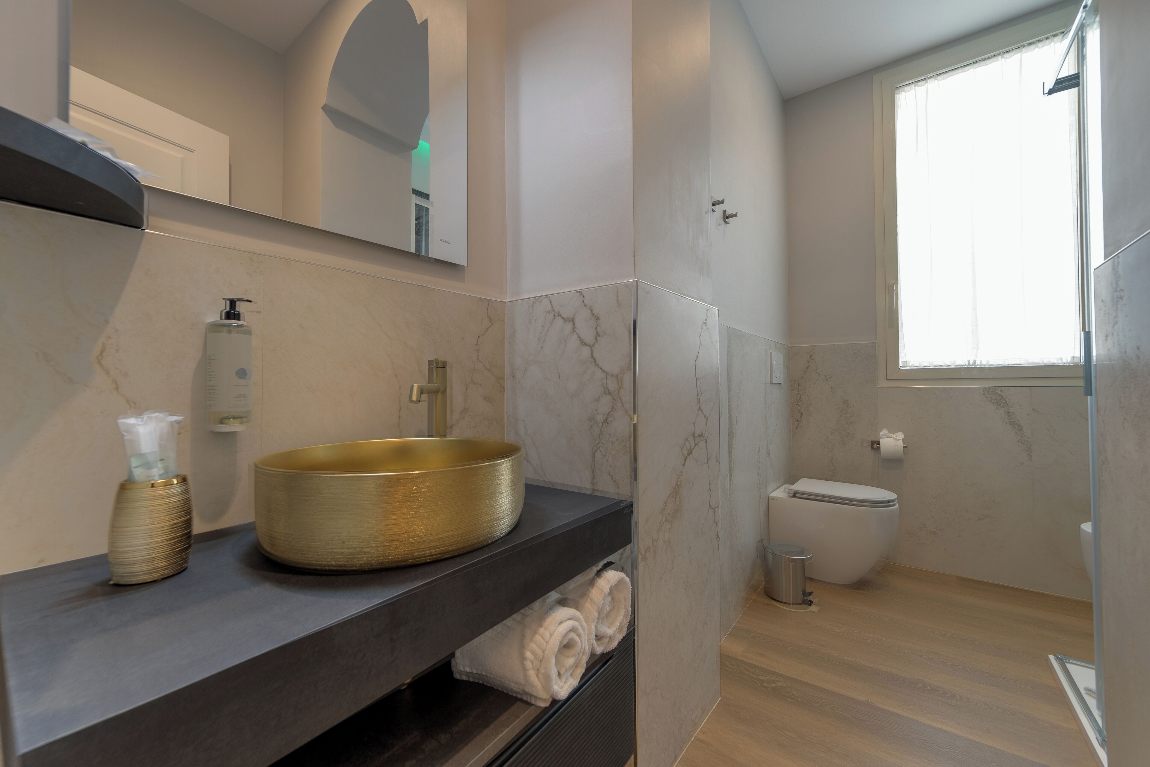 A modern bathroom with a marble vanity, a gold basin, a toilet, and a shower area.
